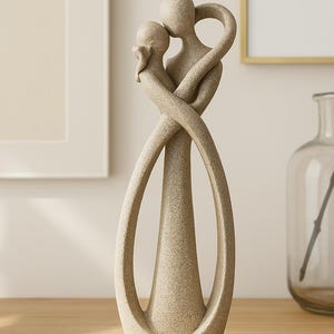 May include: A beige ceramic sculpture of two figures intertwined in an embrace. The sculpture is abstract and modern in style, with the figures' bodies forming a continuous loop.