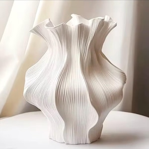 Peut inclure: Un vase en céramique blanc avec un design texturé unique. Le vase a une forme organique et froissée avec des crêtes verticales en forme de vagues. Le vase est sur une surface blanche.