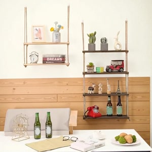 Può includere: Due mensole in legno sospese con oggetti decorativi. La mensola superiore contiene una cornice e un vaso di fiori. La mensola inferiore ha un orologio e libri. L'altra mensola ha cactus, un'auto giocattolo e statuette. Bottiglie e un telefono rosso sono sulla mensola inferiore.