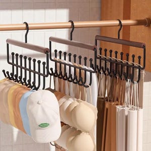 Puede incluir: Organizadores de metal negro para sombreros y accesorios con asas de madera marrón cuelgan de una barra de madera. Los organizadores sostienen gorras de béisbol, sujetadores y otros accesorios. Las gorras son de varios colores.