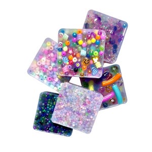 May include: Six square resin art pieces, each filled with colourful beads, shapes, and glitter. The pieces feature pink, purple, blue, green, yellow, and orange. The pieces are arranged in a slightly overlapping pattern. The art pieces are ideal for craft projects.