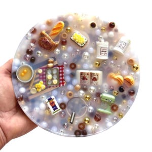 May include: A circular translucent resin tray embedded with miniature kitchen-themed items including a basket of bread, a muffin tin, a green stand mixer, white canisters labeled Sugar and Tea, a bag of flour, and various scattered beads.