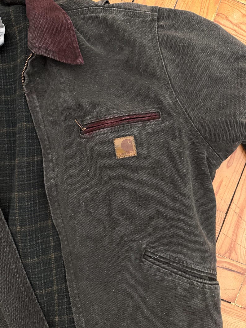 May include: A dark green work jacket with a brown corduroy collar and a Carhartt logo patch on the chest pocket.