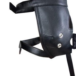 Op de afbeelding: Een zwarte leren harnas met een voorgevormd ontwerp. De harnas heeft een band die om de taille gaat en twee banden die om de benen gaan. De harnas heeft twee zilverkleurige druksluitingen en een kleine opening.