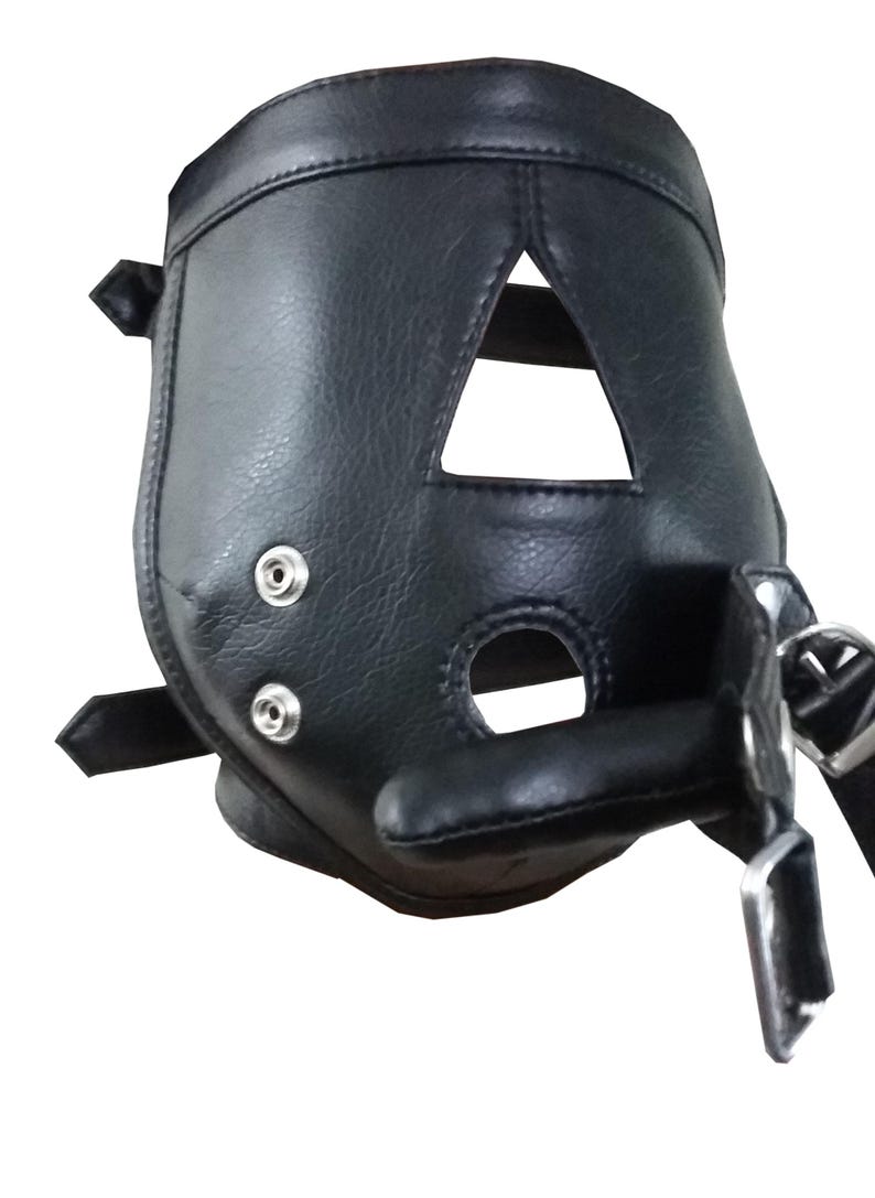 Op de afbeelding: Zwarte leren muilkorf met driehoekige en cirkelvormige openingen. De muilkorf heeft een gewatteerd gedeelte voor de mond en wordt vastgezet met riemen en metalen hardware. Het leer heeft een getextureerde uitstraling.