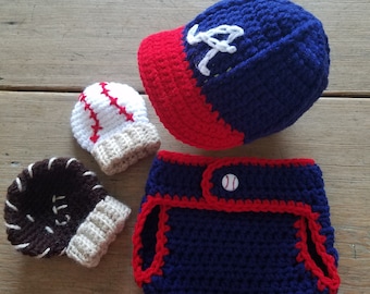Può includere: Un set di abbigliamento per neonati all'uncinetto a tema baseball. Il set include un berretto da baseball blu e rosso con una lettera 'A' bianca sul davanti, un paio di scarpine a forma di guanto da baseball blu e bianche, un paio di scarpine a forma di guanto da baseball marroni e bianche e un pannolino blu e rosso con una palla da baseball bianca sul davanti.