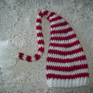 May include: A red and white striped crocheted elf hat with a long, white pom-pom on the end of the hat's tail.