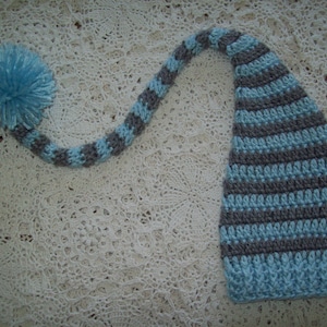May include: A blue and gray striped crocheted elf hat with a long tail and a blue pom-pom on the end.