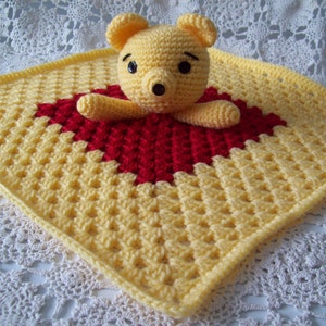 May include: A yellow and red crocheted baby blanket with a crocheted teddy bear in the center.