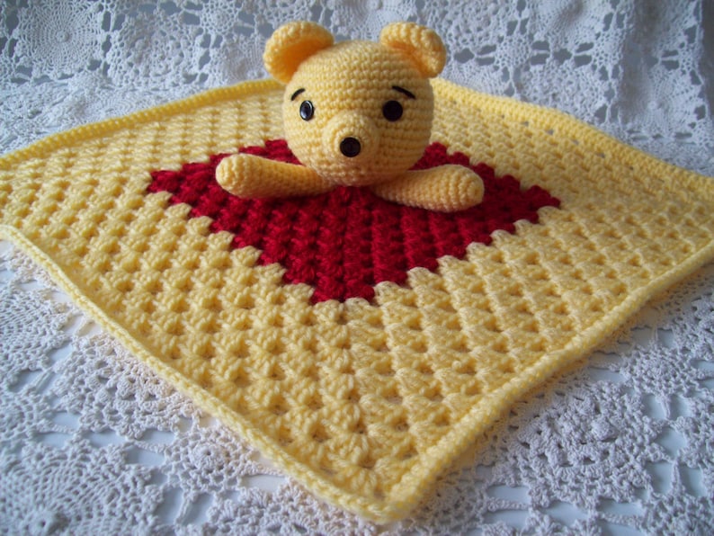 May include: A yellow and red crocheted baby blanket with a crocheted teddy bear in the center.