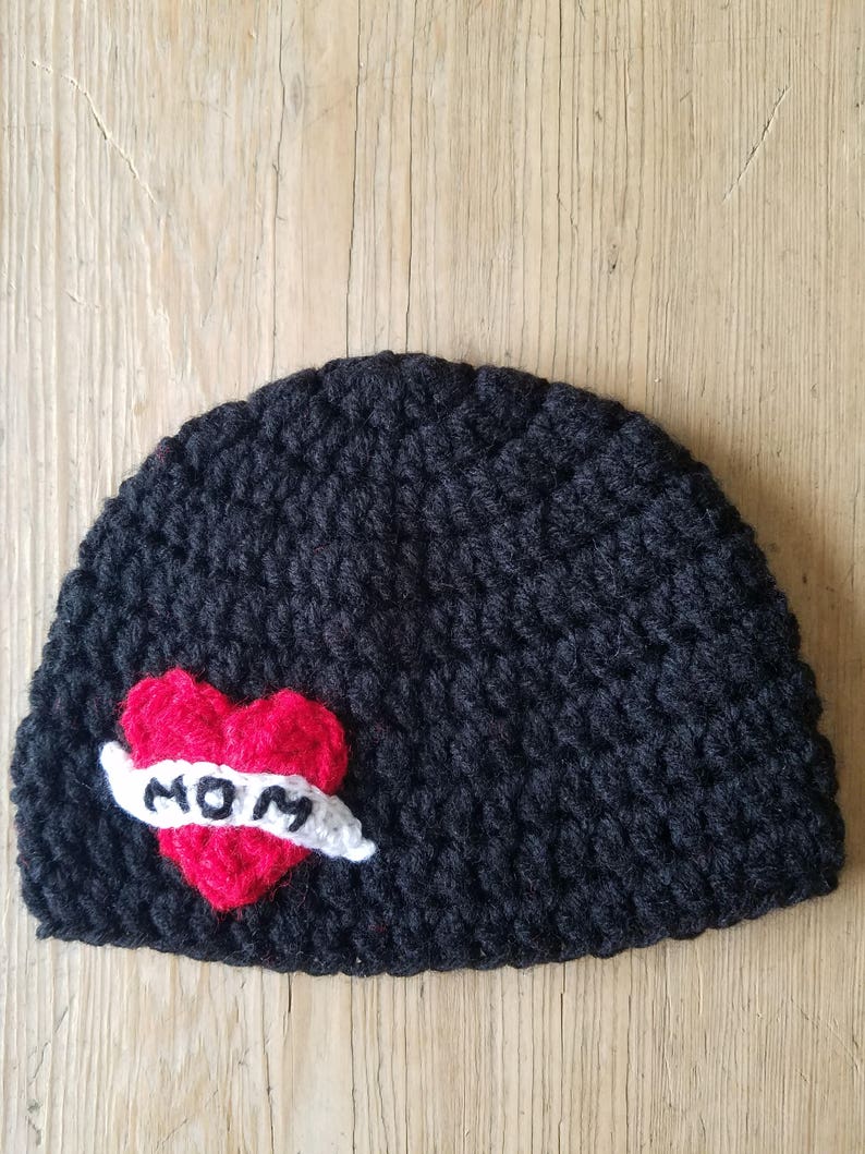 May include: Black crocheted beanie with a red heart and white banner that says "MOM" on it.