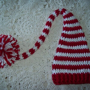 May include: Red and white striped crocheted elf hat with a white pom-pom on the end of the long tail.