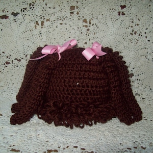 May include: A brown crocheted doll hair wig with two pink bows.