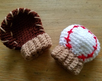 May include: Two crocheted baby booties, one shaped like a baseball with red stitching and a white base, and the other shaped like a baseball mitt with brown stitching and a brown base.