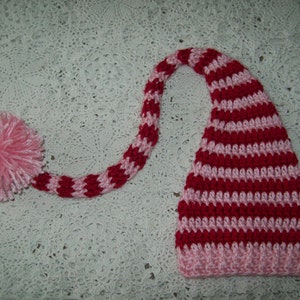 May include: A pink and red striped crocheted elf hat with a long tail and a pink pom-pom.