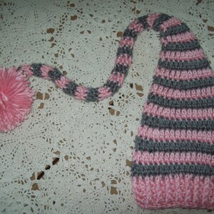 May include: A pink and gray striped crocheted elf hat with a long tail and a pink pom-pom.