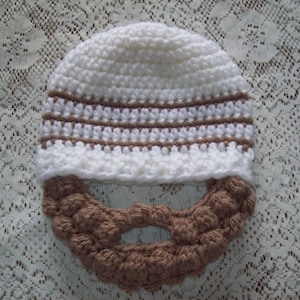 Peut inclure: Un chapeau crocheté blanc avec des rayures marrons et une barbe crocheté marron attachée.