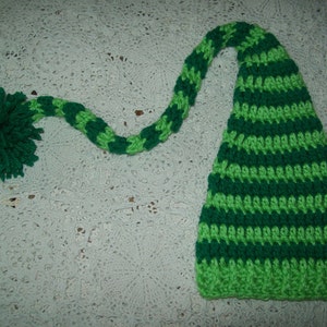 May include: Green and lime green striped crocheted elf hat with a long green and lime green striped tail.