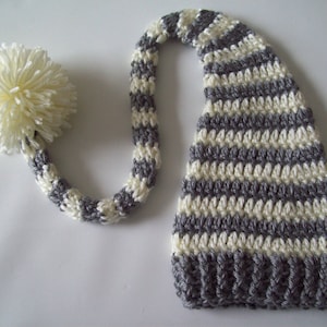 May include: A gray and white striped crocheted elf hat with a white pom-pom on the end of the long tail.