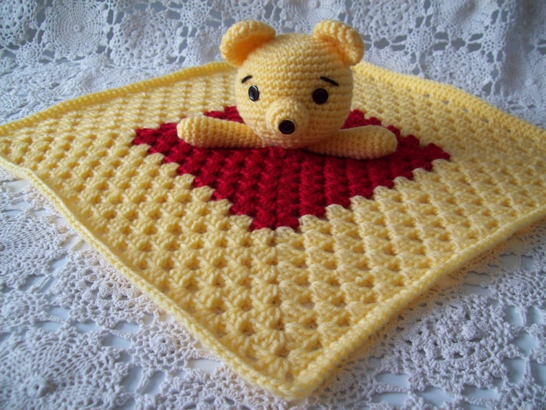 May include: A yellow and red crocheted baby blanket with a crocheted Winnie the Pooh bear in the center.