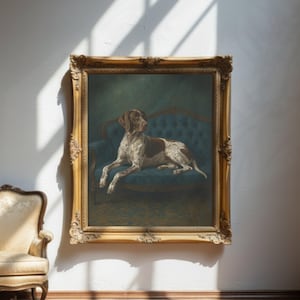 May include: A framed painting of a dog, lying on a blue sofa. The dog has brown and white markings. The ornate gold frame adds a touch of elegance to the artwork. The painting is displayed on a white wall, with sunlight casting shadows.