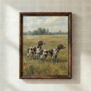 May include: A framed painting showing two brown and white spotted dogs in a field of long grass and wildflowers. The dogs are the main subject, with a landscape of trees, fields, and a cloudy sky in the background. The frame is a dark brown colour.