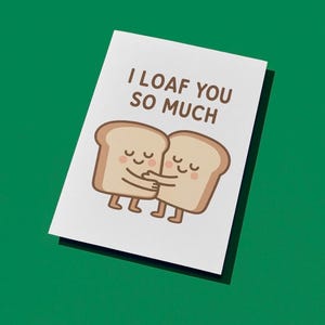 May include: A white greeting card with the text "I loaf you so much" above an illustration of two hugging slices of bread. The bread slices are light brown with smiling faces and small legs. The background is solid green.