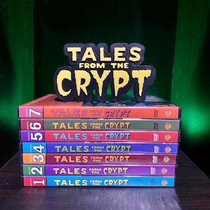 May include: A stack of seven DVD cases for the television series "Tales From the Crypt." Each case is a different color, with the season number on the spine. A black and yellow sign with the show's logo sits on top.