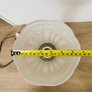 Pu&ograve; includere: Un paralume in vetro smerigliato con bordo smerlato e motivo floreale in rilievo. Il paralume ha un diametro di circa 18 cm. Un metro a nastro giallo &egrave; posto sopra il paralume.