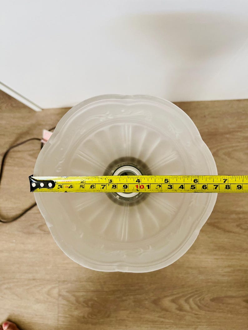 Pu&ograve; includere: Un paralume in vetro smerigliato con bordo smerlato e motivo floreale in rilievo. Il paralume ha un diametro di circa 18 cm. Un metro a nastro giallo &egrave; posto sopra il paralume.