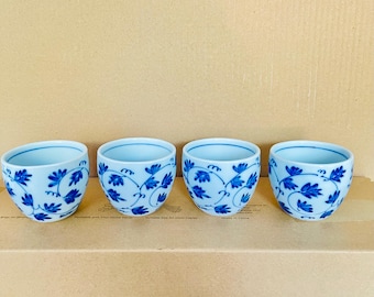 Könnte beinhalten: Vier weiße Keramik-Teetassen mit blauem Blumendesign. Die Tassen haben eine abgerundete Form und sind in einer Reihe angeordnet. Das blaue Blumenmuster ist auf allen vier Tassen einheitlich, mit einem zarten, stilisierten Blatt- und Rankenmotiv.