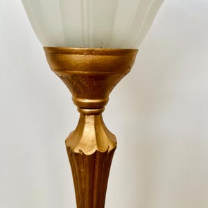 Pu&ograve; includere: Una lampada da terra vintage con base color oro e paralume in vetro bianco scanalato. La lampada presenta un design dettagliato e ornato sulla base e uno stile classico ed elegante. Il paralume &egrave; di colore bianco tenue e la lampada &egrave; probabilmente in metallo.