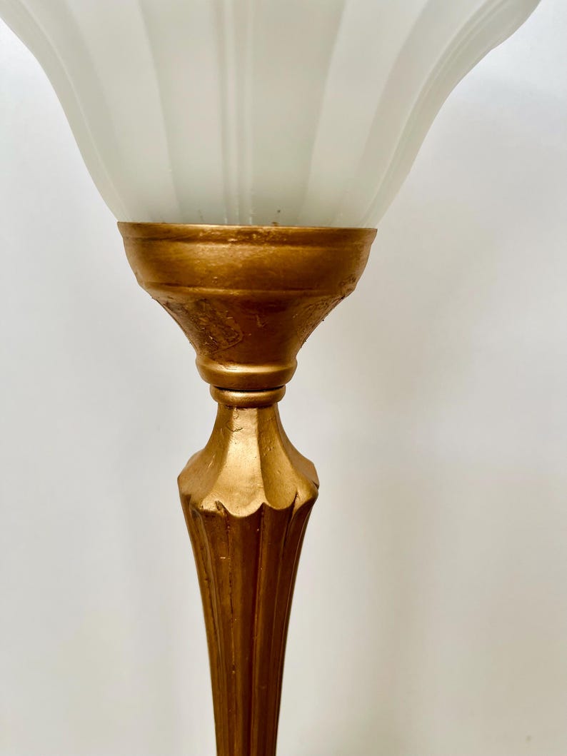 Pu&ograve; includere: Una lampada da terra vintage con base color oro e paralume in vetro bianco scanalato. La lampada presenta un design dettagliato e ornato sulla base e uno stile classico ed elegante. Il paralume &egrave; di colore bianco tenue e la lampada &egrave; probabilmente in metallo.