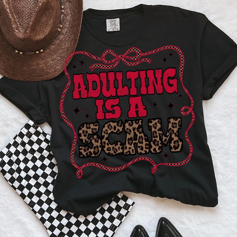 May include: Black t-shirt with the slogan "ADULTING IS A SCAM" in red and leopard print lettering. A brown cowboy hat and black and white chequered shorts are next to the shirt.