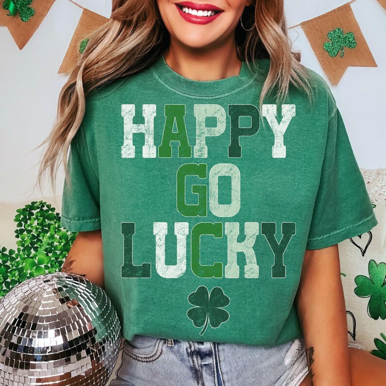 May include: Green t-shirt with the words "HAPPY GO LUCKY" in white and green lettering. A four-leaf clover graphic is below the text. The shirt is a crew neck style.