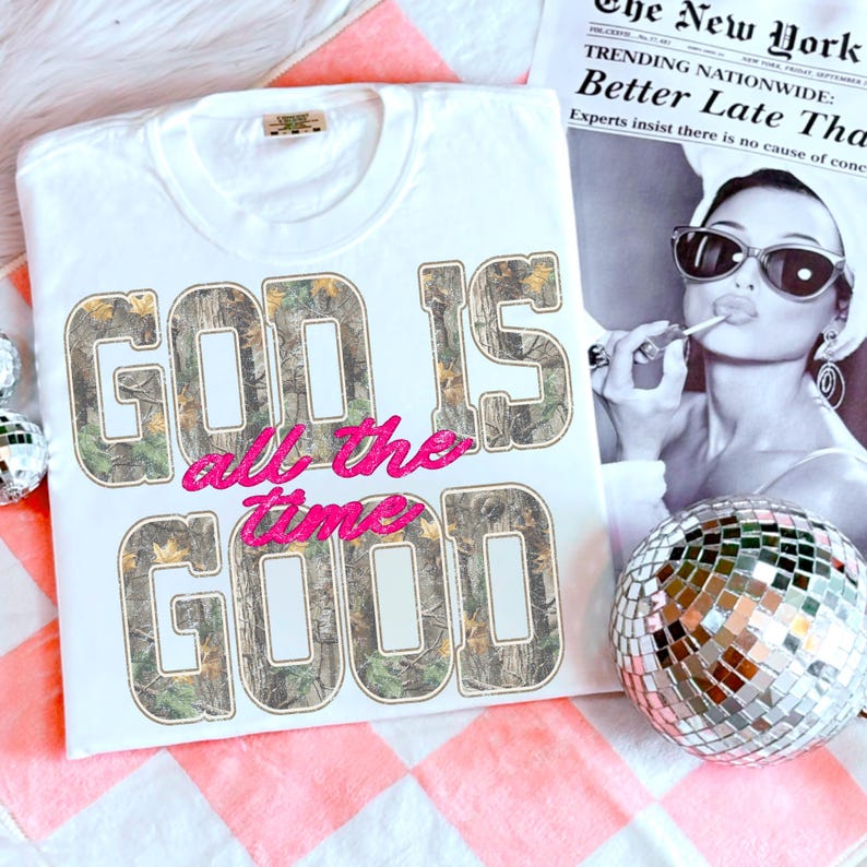 K&ouml;nnte beinhalten: Wei&szlig;es T-Shirt mit dem Text "GOD IS all the time GOOD". Die Buchstaben "GOD IS" und "GOOD" sind mit einem Camouflage-Muster gef&uuml;llt, w&auml;hrend "all the time" in rosa Glitzer gehalten ist. Eine Discokugel und ein Schwarz-Wei&szlig;-Bild befinden sich im Hintergrund.