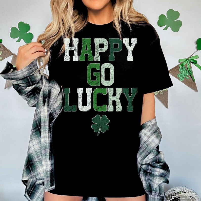 May include: Black t-shirt with the words "HAPPY GO LUCKY" in white and green lettering, and a green shamrock graphic. The shirt is worn with a plaid shirt.