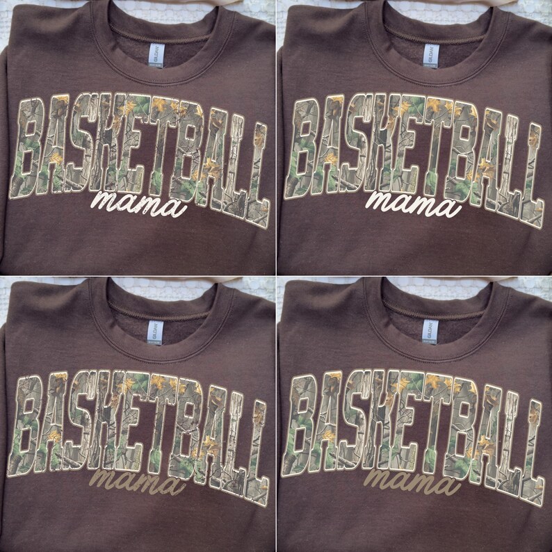 May include: A brown sweatshirt featuring the text "BASKETBALL" in a camouflage pattern and the word "mama" in a cursive font. The sweatshirt is displayed on a wooden hanger.