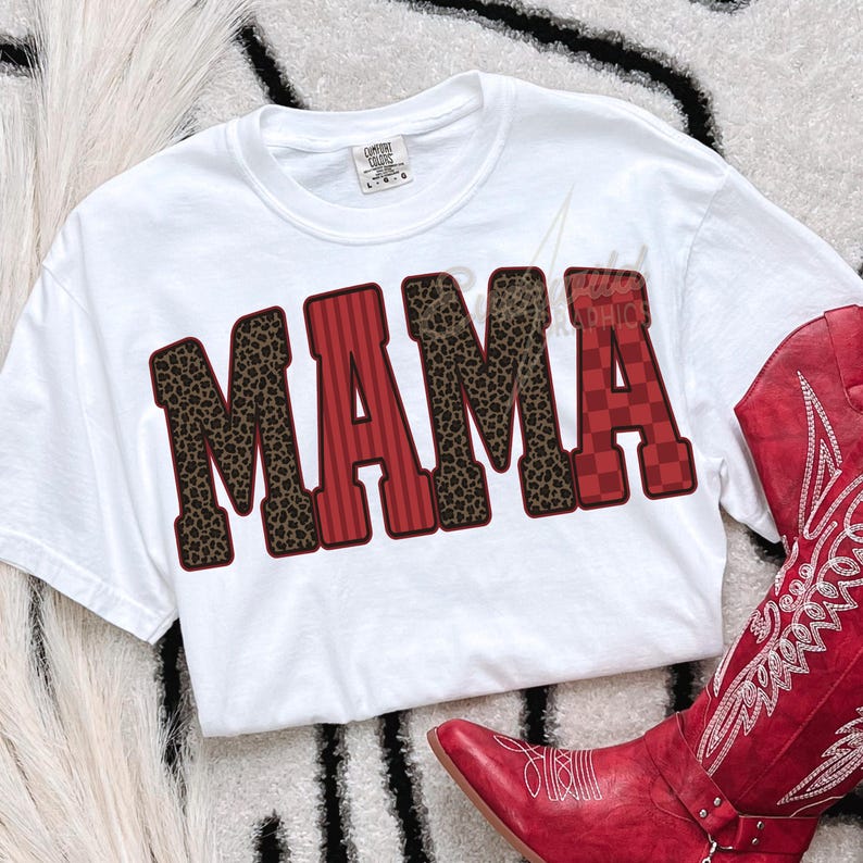 May include: A white short-sleeve t-shirt featuring the word MAMA in large block letters. The letters M, M, and A feature a brown and black leopard print, while the letters A and A feature red vertical stripes and a red checkered pattern.