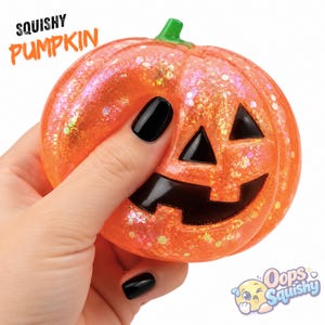 Könnte beinhalten: Ein durchscheinendes, orangefarbenes Squishy-Kürbis-Spielzeug mit eingebettetem, irisierendem Glitzer, einem grünen Stiel und schwarz bemalten Jack-o'-Lantern-Gesichtszügen. Der Text SQUISHY PUMPKIN steht oben links, das Oops Squishy-Logo unten rechts.