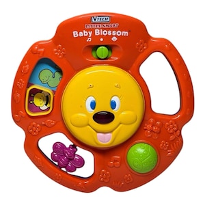 May include: An orange VTech Little Smart Baby Blossom toy. The toy has a yellow smiling face in the center, with blue eyes and a pink tongue. It features a green button, and a small window with a bee and a caterpillar.