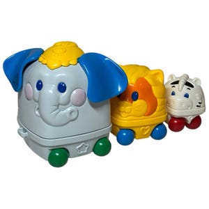 May include: A set of three colorful toy animal figures: an elephant, a lion, and a zebra. The elephant is gray with blue ears, the lion is yellow with an orange mane, and the zebra is white with black stripes. Each toy has wheels.