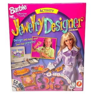 Könnte beinhalten: Eine Barbie Jewelry Designer CD-ROM-Box mit rosa Hintergrund. Die Box zeigt eine Barbie-Puppe, ein Mädchen mit Schmuck und den Text "Entwirf und mache deinen eigenen echten Schmuck!" Das Produkt ist für Kinder ab 8 Jahren geeignet.