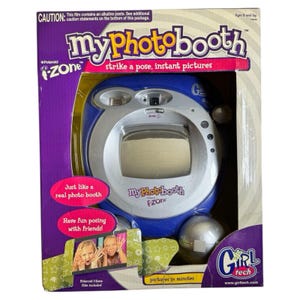 Puede incluir: Una cámara de fotos instantánea My Photo Booth i-Zone azul y plateada. La caja presenta el texto "strike a pose, instant pictures" y "Just like a real photo booth". La cámara está diseñada para mayores de 8 años.