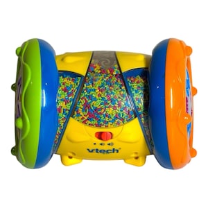 May include: A yellow, blue, green, and orange VTech toy with a clear center filled with colorful beads. The toy has a red button and the VTech logo. The ends are wheels with textured edges.