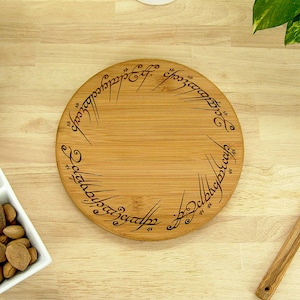 K&ouml;nnte beinhalten: Rundes Servierbrett aus Holz mit eingravierter Schrift am Rand. Das Brett ist aus hellem Holz gefertigt und hat eine nat&uuml;rliche Maserung. Die eingravierte Schrift ist dunkel. Das Brett liegt auf einer Holzoberfl&auml;che.