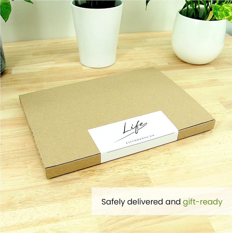 K&ouml;nnte beinhalten: Ein rechteckiger, brauner Karton mit einem wei&szlig;en Etikett mit der Aufschrift "Life LIFEBOARDS UK" in schwarzer Schrift. Die Box steht auf einer hellen Holzoberfl&auml;che, mit zwei wei&szlig;en Topfpflanzen im Hintergrund. Der Text "Safely delivered and gift-ready" steht unten.