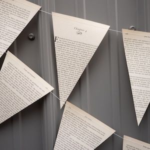 May include: A banner of triangular flags made from pages of a book, strung together with white string. The flags display text from the book, with one flag showing "Chapter 4". The background is a gray, textured surface.