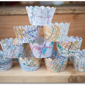 May include: A stack of cupcake liners made from recycled maps. The liners are white with black and blue text and lines. The liners are stacked in a pyramid shape.