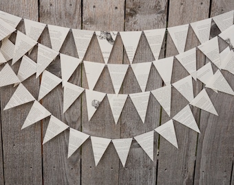 May include: A white paper banner with a triangle shape, made from pages of a book, hangs on a wooden fence. The banner is strung together with white string.
